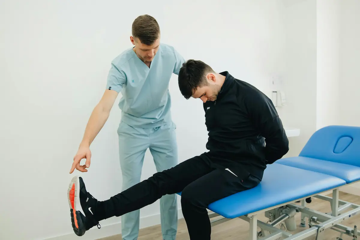 Fisioterapeuta deportivo evaluando la pierna de un corredor en consulta tras una lesión, paciente con zapatillas de running